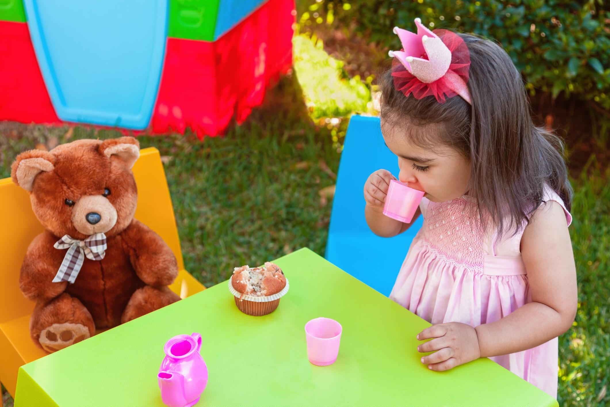 A little girl in pink dress playing house with her brown teddy bear
